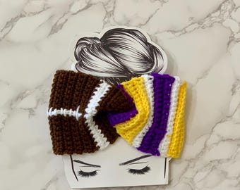 May include: A handmade crochet headband featuring a football design in brown and white, and a section with yellow, purple, and white stripes. The headband is displayed on a card with a hair illustration and drawn eyelashes.