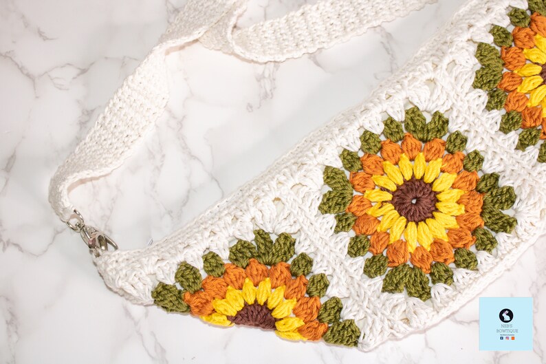 May include: A white crocheted bag with a long strap and a sunflower design. The bag is made with different colored yarn, including green, orange, and yellow.