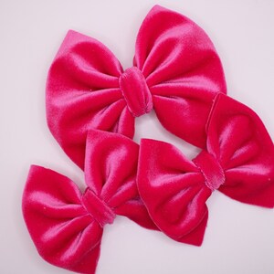 May include: Three pink velvet hair bows of different sizes. The bows are arranged in a triangular shape.