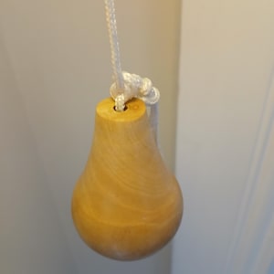 Puede incluir: Un tirador de luz de madera con una perilla en forma de pera y un cordón blanco.