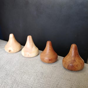 Può includere: Quattro piccoli oggetti in legno a forma di goccia disposti in fila. I due elementi a sinistra sono color marrone chiaro con venature del legno visibili, mentre i due a destra presentano una tonalità marrone rossastra più scura.