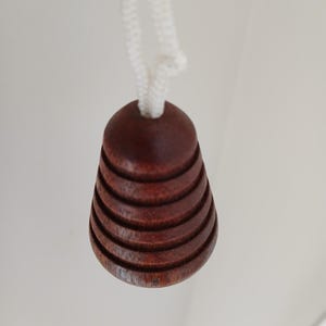 Peut inclure: Un tirette de lumi&egrave;re en bois brun fonc&eacute; avec un design rainur&eacute;, suspendue par un cordon blanc. La tirette a une forme de cloche, avec des rainures horizontales sculpt&eacute;es sur sa surface. Le cordon est nou&eacute; en haut.