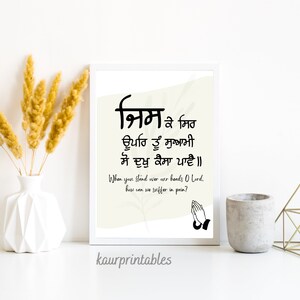 May include: A printable wall art design featuring a Punjabi prayer in black text on a cream background. The prayer reads "निम ३ मित ਊਪਰਿ ਤੂੰ ਸੁਆਮੀ ਸੋ ਦੁਖੁ ਕੈਸਾ ਪਾਵੈ॥" and translates to "When you stand over our hands O Lord, how can we suffer in pain?" The design also includes a black illustration of two hands clasped in prayer.