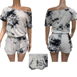 May include: A two-piece tie-dye outfit in white and black. The top is an off-the-shoulder design with short sleeves. The shorts have a drawstring waist. The outfit is made of a soft, lightweight material.