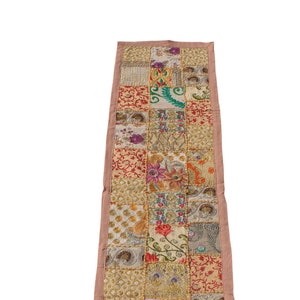 Może przedstawiać: Długi, prostokątny bieżnik stołowy z patchworkowym wzorem. Bieżnik wykonany jest z różnych tkanin w odcieniach złota, czerwieni, różu, zieleni i błękitu. Tkaniny są zszyte ze sobą w losowym wzorze, tworząc unikalny i kolorowy design.