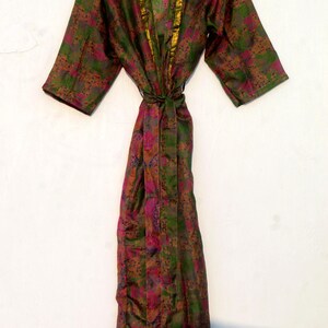 May include: A patterned robe in shades of green, pink, and brown, with gold trim along the collar and sleeves. The robe is tied at the waist with a matching belt. The garment is hanging on a white background.