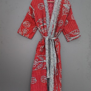May include: A red robe with a floral pattern and gray trim, hanging on a wooden hanger. The robe is tied at the waist with a matching belt. The robe is made of a soft, quilted fabric.