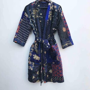 May include: A dark blue patchwork robe with a matching belt, hanging on a wooden hanger. The robe features a variety of colorful floral and geometric patterns in red, gold, and blue. The robe is made of a quilted fabric.