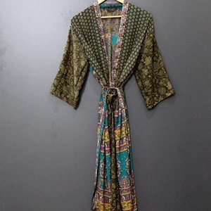 May include: A patterned robe with a tie waist hangs on a wooden hanger. The robe features a mix of colors, including green, teal, and purple, with floral and geometric designs. The sleeves are three-quarter length.