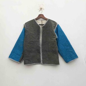 May include: A quilted jacket with a V-neck design. The jacket has a grey body and blue sleeves. White stitching outlines the seams and edges. The jacket is hanging on a wooden hanger against a white background.