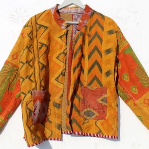 Op de afbeelding: Een geel, oranje en groen patchwork jack met een geometrisch patroon. Het jack heeft een mandarijnkraag en een knoopsluiting. Het heeft twee zakken aan de voorkant.