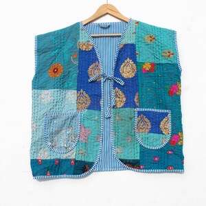 May include: A patchwork vest in shades of teal, blue, and gold, with floral and paisley patterns. The vest has two front pockets and a striped lining. It is sleeveless and has a tie closure at the front.