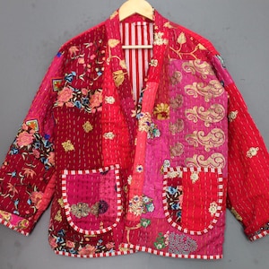 May include: A patchwork jacket in shades of red and pink, featuring floral and cloud-like patterns. The jacket has two front pockets and a striped lining. The design is a mix of textures and colors, creating a unique and artistic look.