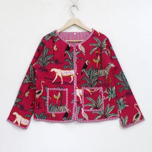 May include: A long-sleeved quilted jacket in a vibrant magenta pink featuring a repeating jungle print with leopards, zebras, toucans, and palm trees. The jacket has a round neckline, a front button closure, and two square front pockets.