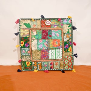 Puede incluir: Un cojín de suelo cuadrado verde con un diseño de patchwork. El cojín está hecho de diferentes telas y colores, incluyendo rojo, rosa, amarillo, azul y verde. El cojín tiene borlas en cada esquina.
