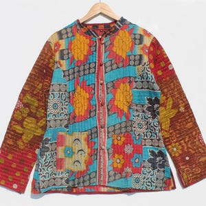 May include: A colorful, quilted jacket with a mandarin collar. The jacket features a patchwork design with floral and geometric patterns in shades of red, blue, yellow, and brown. It has long sleeves and a button-up front.