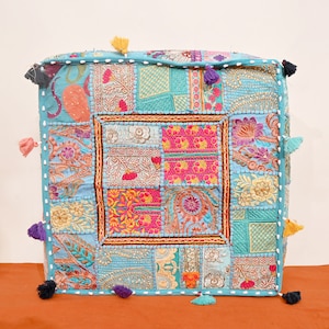 Puede incluir: Un cojín cuadrado de patchwork azul y blanco con bordados coloridos y borlas. El cojín está hecho de varias telas y tiene un estilo único y bohemio.