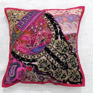Puede incluir: Una almohada cuadrada de patchwork con un diseño floral rosa, morado, negro y dorado. La almohada está hecha de diferentes telas y tiene un borde rojo.