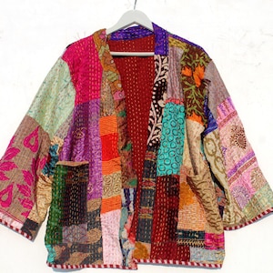 Puede incluir: Una chaqueta de patchwork colorida con forro rojo y un frente largo y abierto. La chaqueta está hecha de varias telas y tiene un estilo único y bohemio.