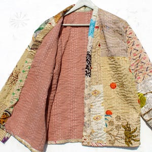 Könnte beinhalten: Eine Patchwork-Steppjacke mit rosa Futter. Die Jacke besteht aus verschiedenen Stoffen in Beige-, Braun- und Weißtönen. Der Stoff hat ein Blumenmuster und ein geometrisches Design.
