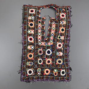Könnte beinhalten: Ein Vintage-Textil mit rechteckiger Form und Halsausschnitt. Das Textil weist aufwendige Stickereien mit farbenfrohen kreisförmigen und geometrischen Mustern, einschließlich Spiegeln, auf. Die dominierenden Farben sind Braun, Schwarz, Rot und Lila.