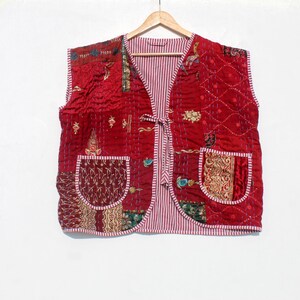May include: A quilted red vest with a striped interior and two front pockets. The vest features decorative stitching and patches of patterned fabric in shades of gold, green, and burgundy. It hangs on a wooden hanger.