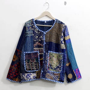 May include: A blue patchwork jacket with a V-neck and two pockets. The jacket is made of different fabrics and has a quilted design.