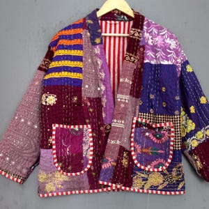 May include: A patchwork jacket with a variety of colors, including purple, orange, and burgundy. The jacket has two pockets and is decorated with floral embroidery and sequins. The lining is striped red and white.