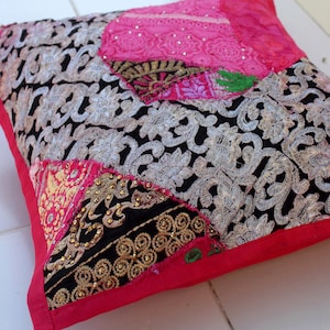 May include: A pink and black patchwork pillow with intricate embroidery and gold accents. The pillow is made of various fabrics and has a unique, bohemian style.