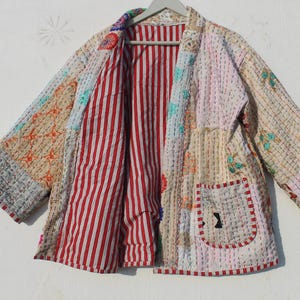 Puede incluir: Una chaqueta acolchada de retazos con forro de rayas rojas y blancas. La chaqueta tiene un bolsillo grande en la parte delantera y está hecha de una variedad de telas.