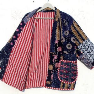 Pode incluir: Uma jaqueta acolchoada azul e vermelha com um design de patchwork. A jaqueta tem manga comprida e um bolso do lado esquerdo. A jaqueta é feita de uma variedade de tecidos e tem um visual único e feito à mão.