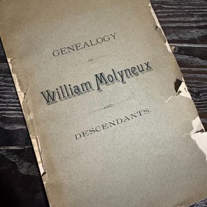 May include: An antique book titled "Genealogy of William Molyneux and Descendants." The cover is a faded tan color with black text. The edges of the book are torn and worn, suggesting age and use.