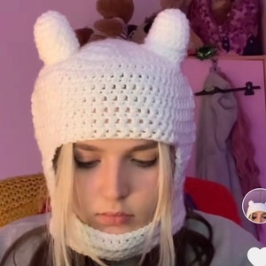 May include: White crocheted hat with ear flaps and a face mask. The hat has a textured knit pattern and is designed to cover the head and neck.