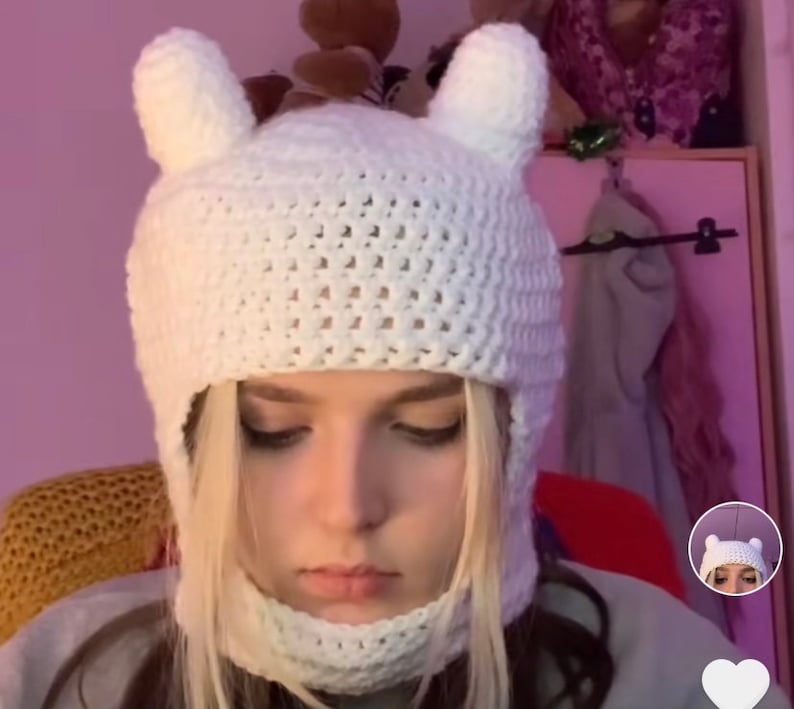May include: White crocheted hat with ear flaps and a face mask. The hat has a textured knit pattern and is designed to cover the head and neck.