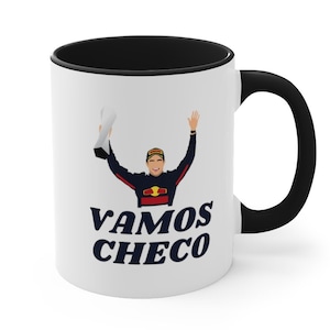 May include: White ceramic mug with a black rim and handle. The mug features a cartoon illustration of a race car driver holding a trophy and the text "VAMOS CHECO" in blue.