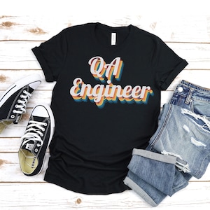 May include: A black t-shirt with a retro-style graphic that says "QA Engineer" in rainbow colors.
