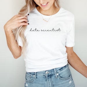 May include: White t-shirt with the words "data scientist" in a black, handwritten font. The shirt is a crew neck style and is paired with blue denim jeans. The overall aesthetic is casual and modern.