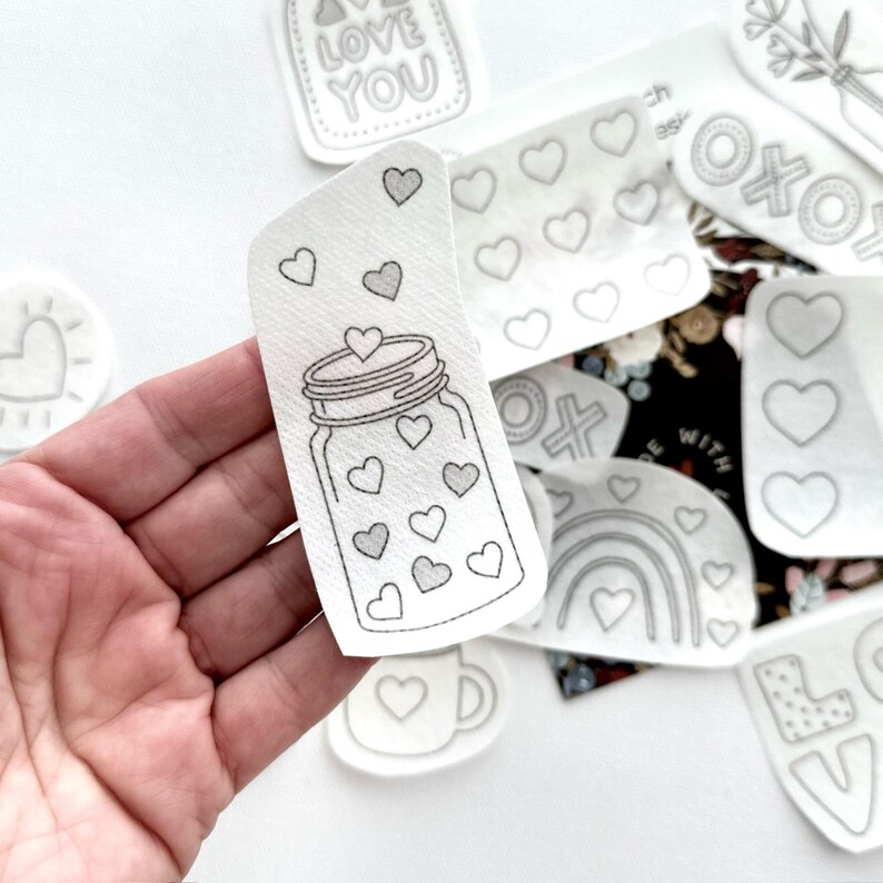 May include: A white iron-on patch with a black outline of a mason jar filled with hearts. The patch is perfect for adding a touch of love to any project.