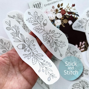 May include: A set of six white fabric embroidery patterns featuring a floral design with leaves, berries, and acorns. The patterns are labeled "Stick and Stitch".