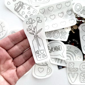 May include: A set of iron-on patches featuring various Valentine's Day themes, including a vase of flowers, a heart-shaped mug, and the words "Be Mine!" and "XOX".