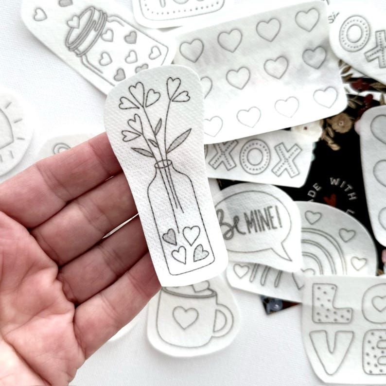 May include: A set of iron-on patches featuring various Valentine's Day themes, including a vase of flowers, a heart-shaped mug, and the words "Be Mine!" and "XOX".