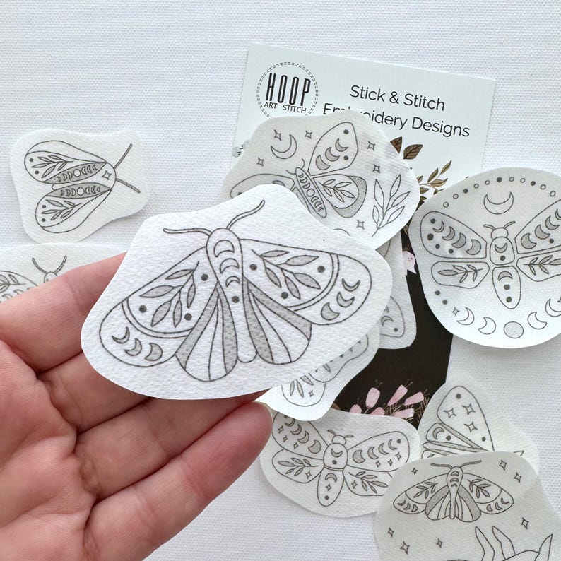 May include: A set of 8 iron-on transfer designs featuring moths with intricate patterns and details. The designs are printed on white fabric and are ready to be ironed onto fabric for embroidery projects.