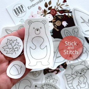Pode incluir: Um conjunto de padrões de bordado de feltro branco com temas de animais e natureza, incluindo um urso, um coelho, um guaxinim, uma folha e uma bolota. Os padrões são etiquetados como "Stick and Stitch".