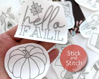 May include: A set of iron-on patches with fall-themed designs, including a pumpkin, a leaf, and the text "hello fall". The patches are white with black outlines and are designed for stick and stitch crafts.