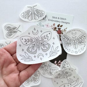 May include: A set of five embroidery patterns featuring moths with moon and star details. The patterns are printed on white paper and labeled "Stick & Stitch Embroidery Designs".