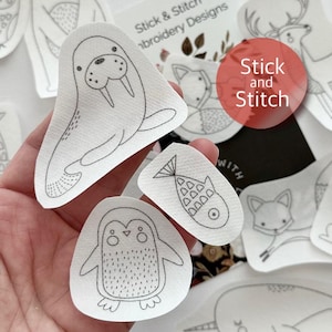 May include: A set of white fabric patches with black line drawings of various animals, including a walrus, penguin, fish, fox, and deer. The patches are labelled "Stick and Stitch".