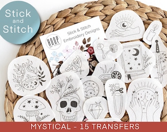May include: A set of 15 iron-on embroidery transfers with mystical designs. The designs include a skull, a potion bottle, a mushroom, a crescent moon, a book, a diamond, a hand holding a crystal ball, and more. The transfers are on white fabric and are ready to be ironed onto fabric.