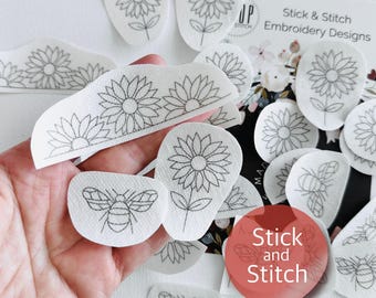Puede incluir: Una colección de diseños de bordado preimpresos en blanco con girasoles y abejas. Los diseños están delineados con tinta negra e incluyen el texto "Stick & Stitch Embroidery Designs".