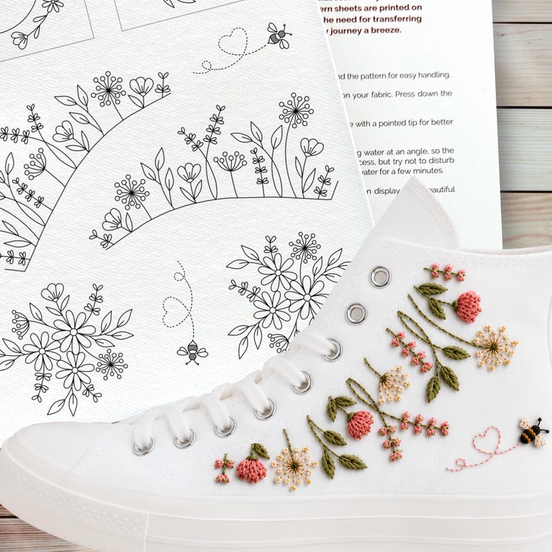 Puede incluir: Una zapatilla de lona blanca de ca&ntilde;a alta con un intrincado bordado floral en hilo rosa, amarillo y verde, junto a un peque&ntilde;o motivo de abeja y coraz&oacute;n. Junto al zapato hay una hoja de instrucciones con patrones florales en l&iacute;nea negra.