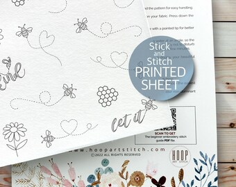 May include: A white printed sheet with a bee and honeycomb design. The sheet has the text "Stick and Stitch your beautiful PRINTED SHEET" and "let it" on it. The sheet is folded over a floral pattern.
